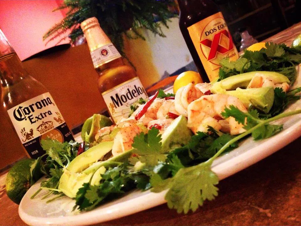 A plate of shrimp with avocado and cilantro next to bottles of Mexican beer